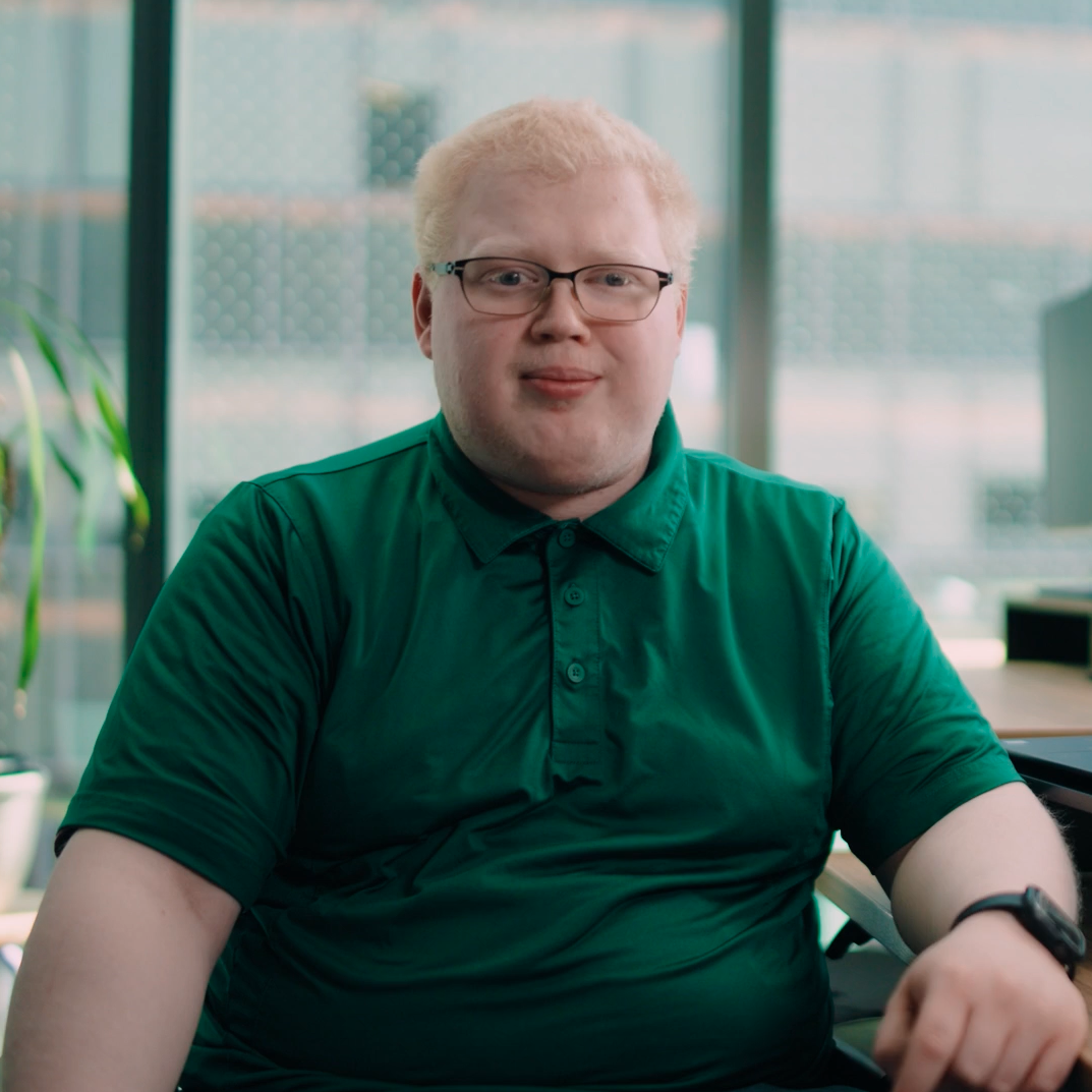 Andrew, a white man with light hair and glasses, seated at an office desk with large windows in the background
